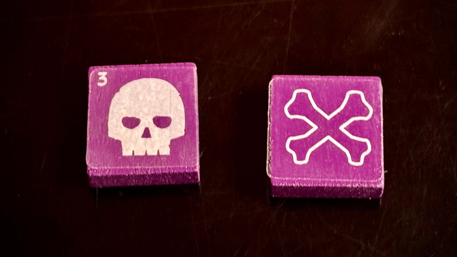 A hand flipping a QuoDrox tile to reveal the crossbones side, showing a dead creature