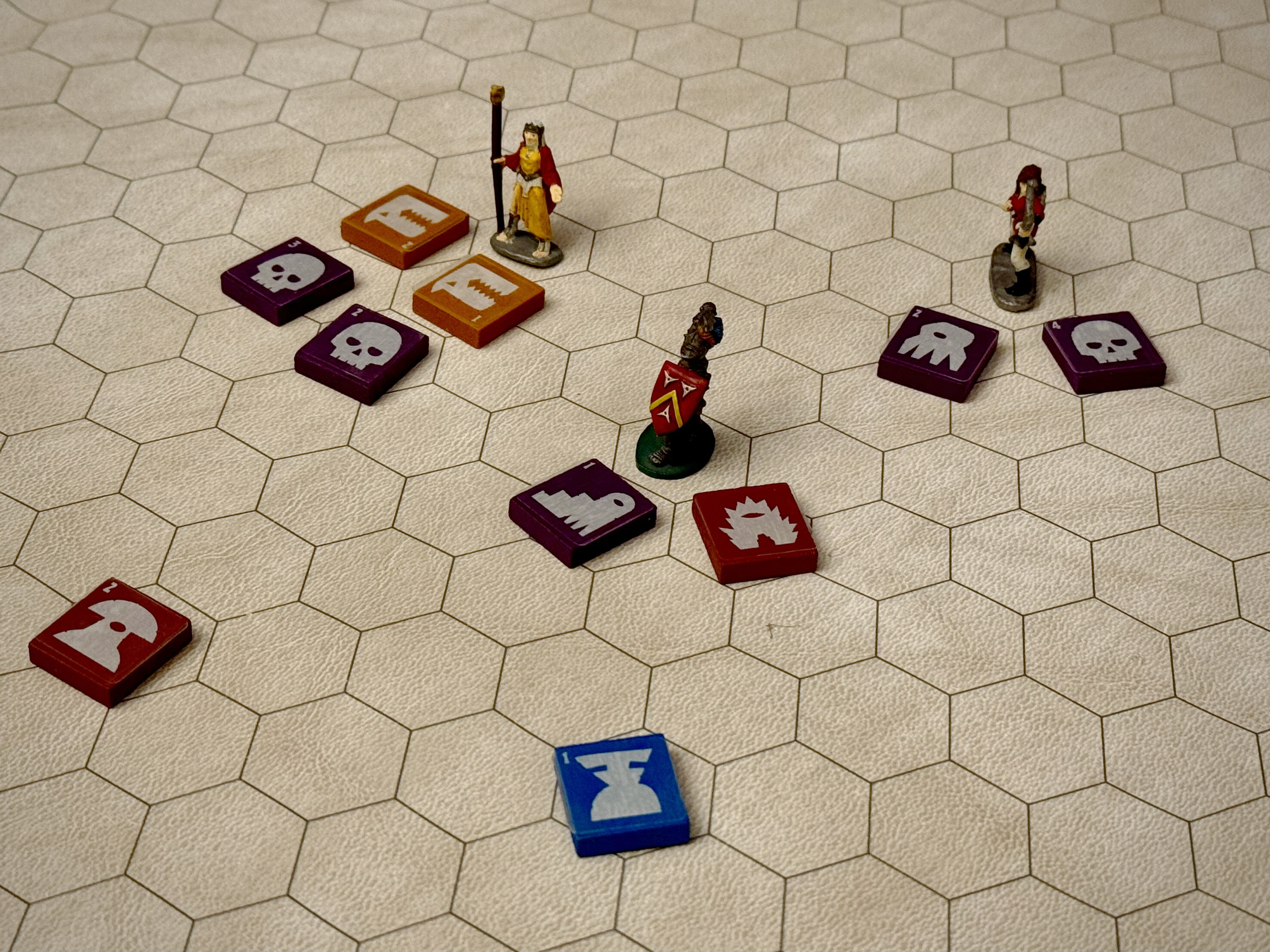 QuoDrox creature tiles arranged on a hex battle map alongside miniature figures, showing tiles in purple, red, and blue